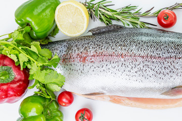 Raw sliced trout next to an assortment of red and green vegetables, lemons and rosemary. Top view.