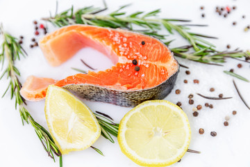 Uncooked trout sliced in the form of a steak. With lemons and condiments on the side.