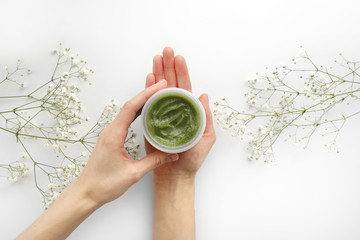Young Female hands hold a jar of green natural cream for face or body. organic natural skincare products and flower on white. Packaging of lotion or cream. Beauty cosmetic skincare concept.
