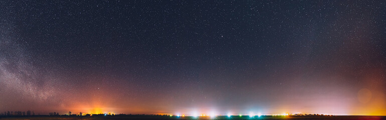 Night Starry Sky With Glowing Stars Above Countryside Landscape. Milky Way Galaxy And Rural Field Meadow In Early Spring. Panorama, Panoramic View