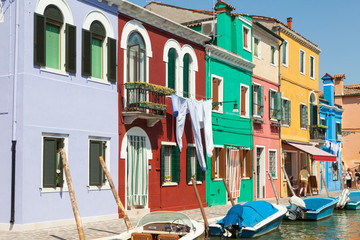 Fototapeta na wymiar Row of brightly coloured houses, Burano, Venice, Italy with laundry drying overlooking a canal with boats