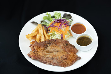 Beef steak with barbecue and paper sauces, side dish salad and french fries  served on white plate, black background .