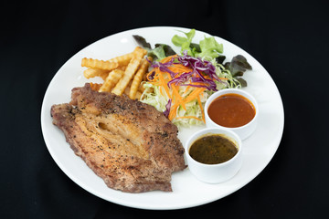 Beef steak with barbecue and paper sauces, side dish salad and french fries  served on white plate, black background .