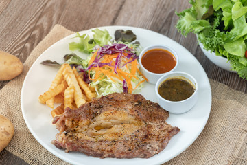 Beef steak with barbecue and paper sauces, side dish salad and french fries  served on white plate, wooden table.