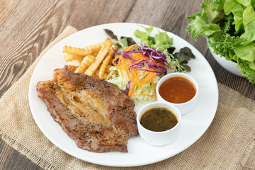 Beef steak with barbecue and paper sauces, side dish salad and french fries  served on white plate, wooden table.