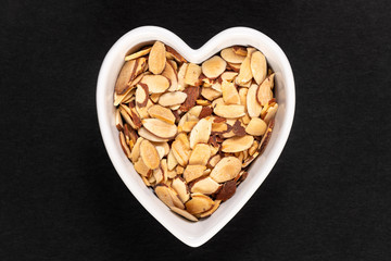A roasted pile of sliced almonds in a heart-shaped bowl isolated on a back background.