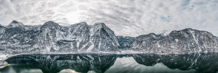 Aerial panoramic drone shot of snow mountains around Lahn, Hallstatt, Obertraun village by lake in winter overcast time in Austria