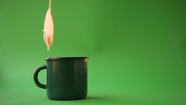 tea-making - a tea bag of 100% cotton on a rope appears on the screen and swings over a green mug with hot water on a green background, steam coming from the mug. the concept of natural tea packs.