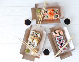 Flat lay composition with sushi rolls, chopsticks, marinated ginger, soy sauce, wasabi in eco boxes on white wooden table. Food delivery and takeaway concept © Дмитрий Сидор
