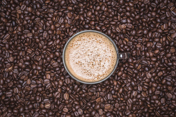 Cup of cappuccino placed in a plate of coffee beans, with Roasted Full frame coffee beans background