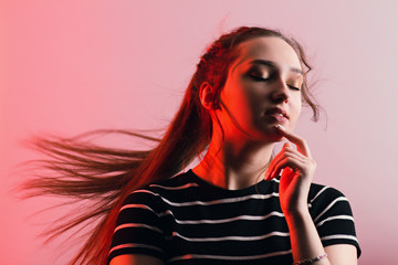 portrait of a beautiful sensual girl with makeup and with flying long hair on studio red background, concept beauty and fashion