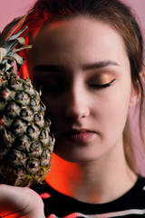 portrait face of a beautiful girl with makeup and and pineapple fruit on red background, woman closed eyes near peel texture, concept female beauty and natural vitamins