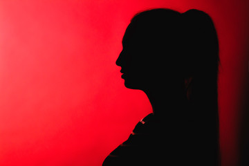 silhouette of thoughtful girl on red lightened background, unrecognizable woman face profile, concept emotions, stress