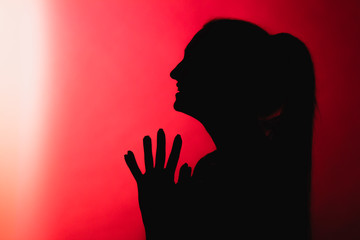 silhouette of malevolent girl on red lightened background, unrecognizable woman face profile, concept emotions