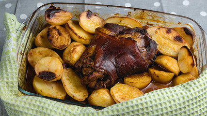 Roast pork knuckle in the oven. Meat and fried potatoes. Homemade food. Glass dish for the oven. Fork and knife.