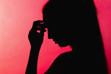 silhouette of upset worried girl with hand on forehead, unrecognizable woman face profile on red background, concept life problems, anxiety,destructive emotions