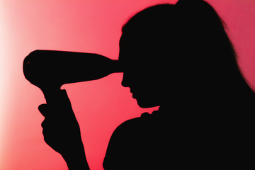silhouette of a beautiful woman profile doing a hairstyle with hair dryer on red background, concept of beauty and danger