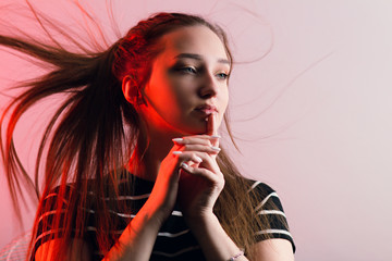 portrait of a beautiful sensual girl with makeup and with flying long hair on studio red background, concept beauty and fashion