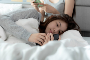 Two asian friend ship women stay home lying in room,like lovely lesbian couple. hold hand phone connect on line.