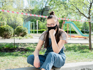 A teenage girl is sitting on the background of the Playground is fenced red lantow during a pandemic coronavirus.