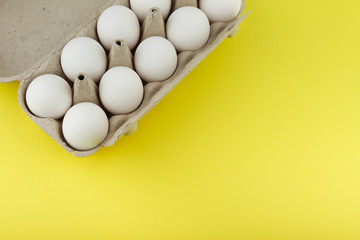 white chicken eggs in a cardboard  egg box on a yellow background top view with copy space