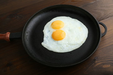 two fried eggs is in the pan on dark wooden background