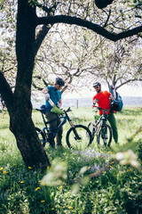 Two mountain bikers resting and prepare stuff during riding.in the spring forest. The sun is shining through the flowering trees. Bikepacking and touring concept