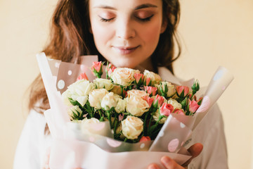 Young beautiful woman with roses bouquet close up on beige background. Soft tender colors. 