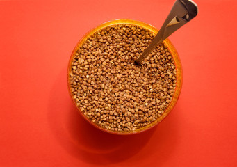 raw buckwheat in a plastic container with a spoon on a red background