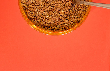 raw buckwheat in a plastic container with a spoon on a red background