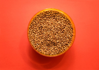 uncooked buckwheat in a plastic container on a red background