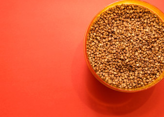 uncooked buckwheat in a plastic container on a red background