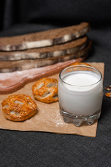 Baking, dark bread, cookies and rolls on a dark background.
Kraft paper. Milk in a transparent glass.