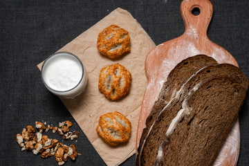 Baking, dark bread, cookies and rolls on a dark background.
Kraft paper. Milk in a transparent glass.