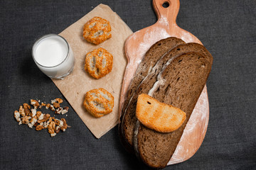 Baking, dark bread, cookies and rolls on a dark background.
Kraft paper. Milk in a transparent glass.