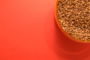uncooked buckwheat in a container on a red background in the corner
