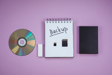 dvd, flash drive, hard drive, sd card and Notepad with the words backup are on a lilac background.