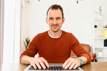 Webcam view of attractive guy in casual wear at home, he is typing on the keyboard and watching on the screen. Web surfing, develop, freelance, video call