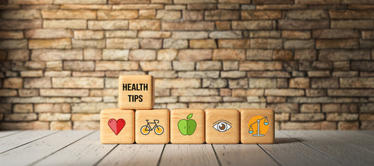 cubes with text HEALTH TIPS and health icons in front of a brick wall on a wooden floor