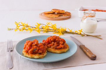 Table with homemade spicy baked beans with bacon and potato crumpets, cup of coffee, glass of cream, embellished with few twigs of golden rain. English breakfast.