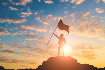 Silhouette of victory businessman on mountain with city light background. Business success and...