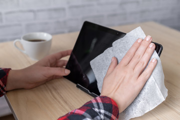 A woman worker cleaning with antivirus wet wipe a tablet and a working office desk before starting...