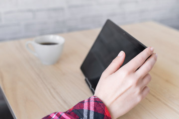 Obraz premium Woman using a tablet while sitting at a table in a cafe and drinks coffee