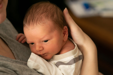 Tiny caucasian newborn baby boy resting in mothers arms after breastfeeding session. Baby with yellow skin because of baby jaundice, typical condition for first days of newborns life.