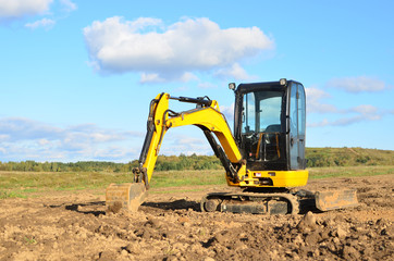 Mini excavator digging earth in a field or forest. Laying underground sewer pipes during the...