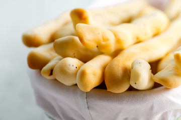 Traditional Italian bread sticks with poppy in a basket on a white wooden background.