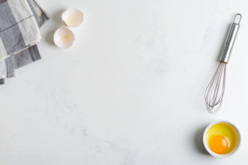Yolk in bowl and metal whisk on a stone kitchen table.
