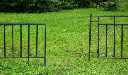 A metal fence with a broken gate on the green grass