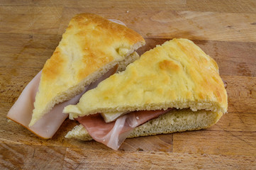 Slice of italian focaccia bread stuffed with speck ham and taleggio cheese on wooden cutting board.