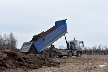 Obraz premium Dump truck dumps its load of sand and ground on construction site for road construction or for foundation work. Transportation of bulk cargo. Trucking industry, freight cargo transport